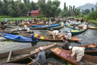 श्रीनगर में डल झील पर एक अस्थायी बाजार में सब्जियां बेचने के लिए ग्राहकों की प्रतीक्षा करते किसान और व्यापारी